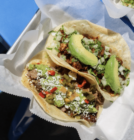 Two tacos on white paper—one with ground meat, cilantro, onion, and avocado; the other with beef, guacamole, red peppers, corn, cotija cheese, and avocado. A delicious find among healthy places to eat in Austin. Austin Marathon Half Marathon & 5K